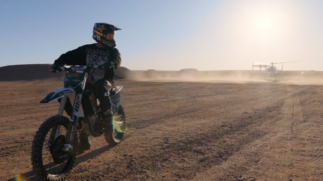 A person on a motorbike with a helicopter in the background