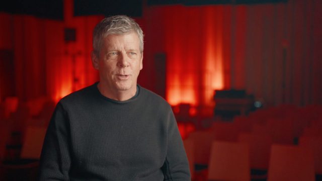 Peter Deming talking in front of a red background